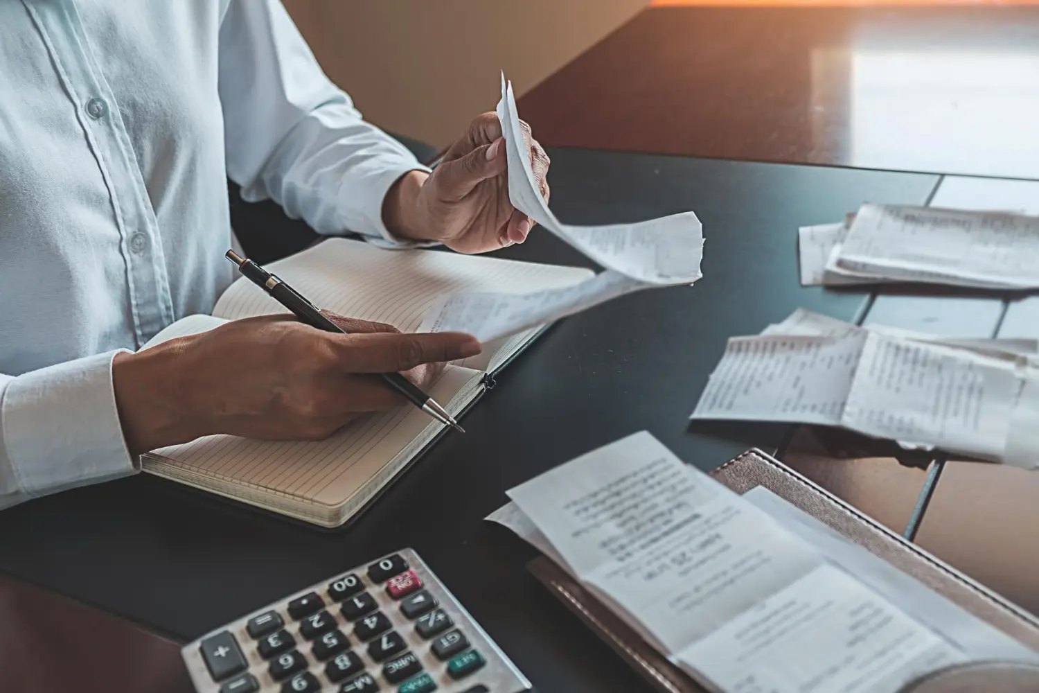 Mãos conferindo recibos e calculadora para controle de notas fiscais