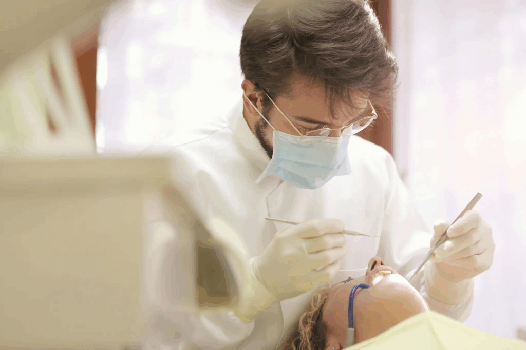 Dentista usando máscara, óculos e luvas realiza atendimento odontológico em uma paciente deitada na cadeira do consultório.
