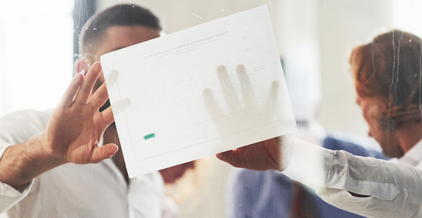 Pessoas em reunião observam um documento colado ou segurado contra uma superfície de vidro, com mãos apontando e interagindo com o material.