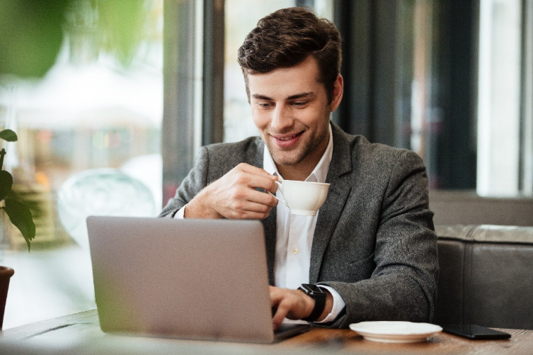 Homem de meia idade utilizando um notebook e tomando um café.