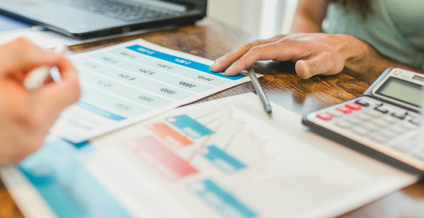 Mãos analisam planilhas e documentos fiscais com calculadora para novos padrões NF-e/NFC-e e reforma tributária.