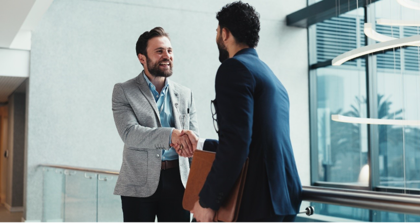 Dois homens (empresários) apertam as mãos. Ambos estão sorrindo e felizes.