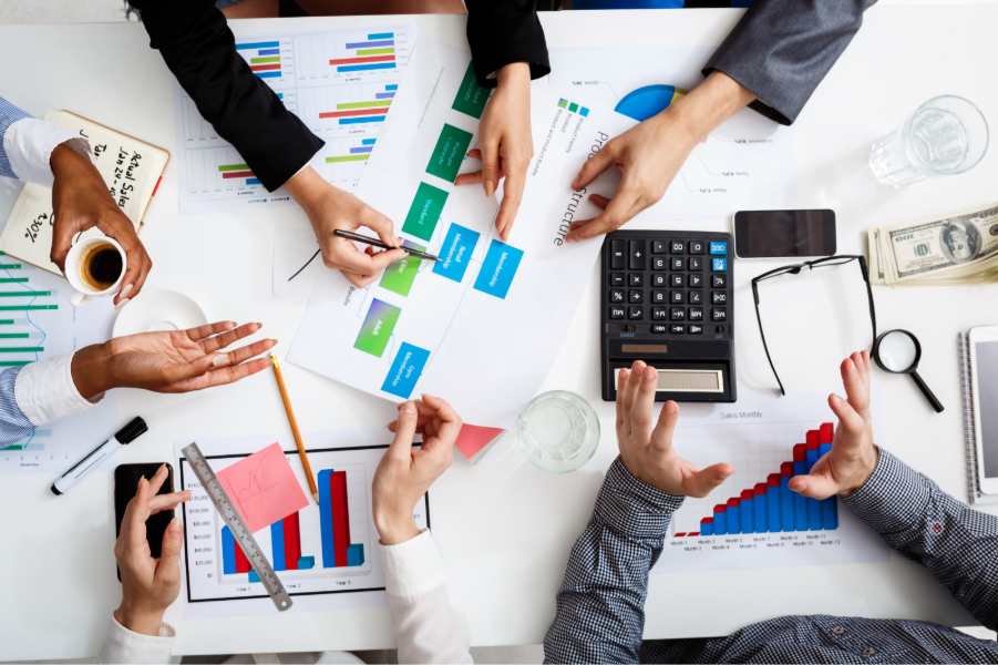 Equipe analisando gráficos financeiros e documentos em mesa de reunião com calculadora, relatórios de desempenho e planejamento estratégico empresarial.